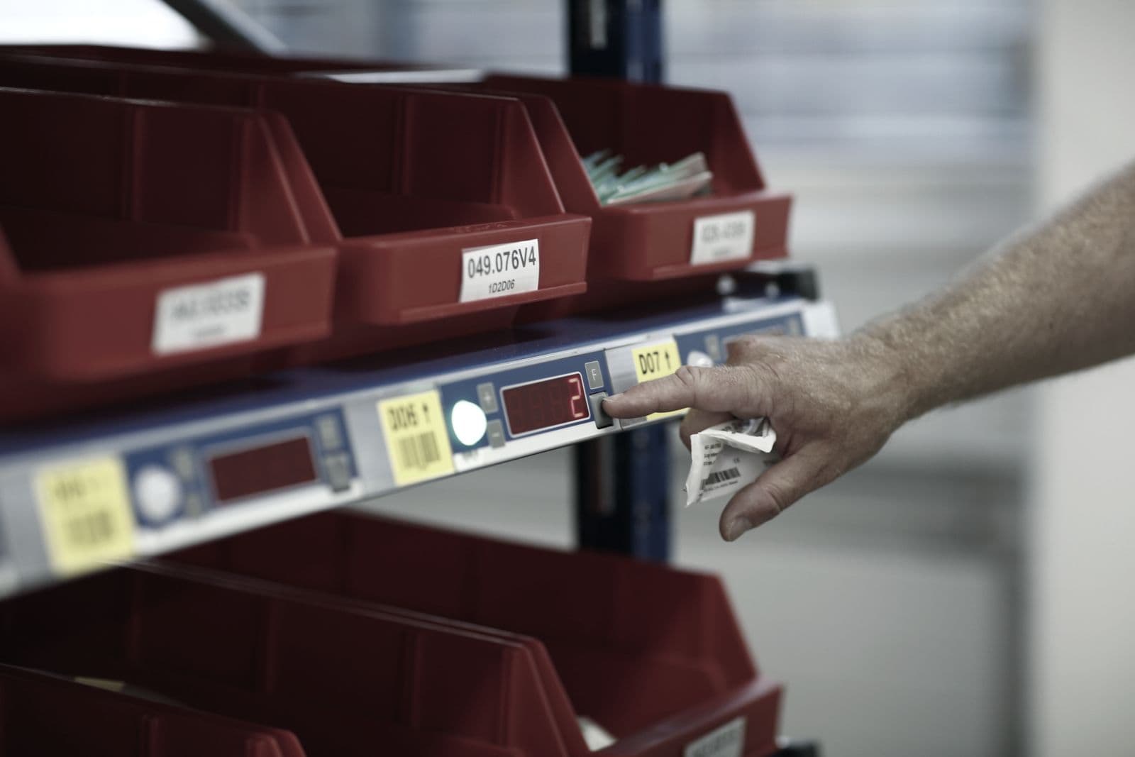 Mano pulsando un indicador pick-to-light en una estantería de cubetas de preparación de pedidos