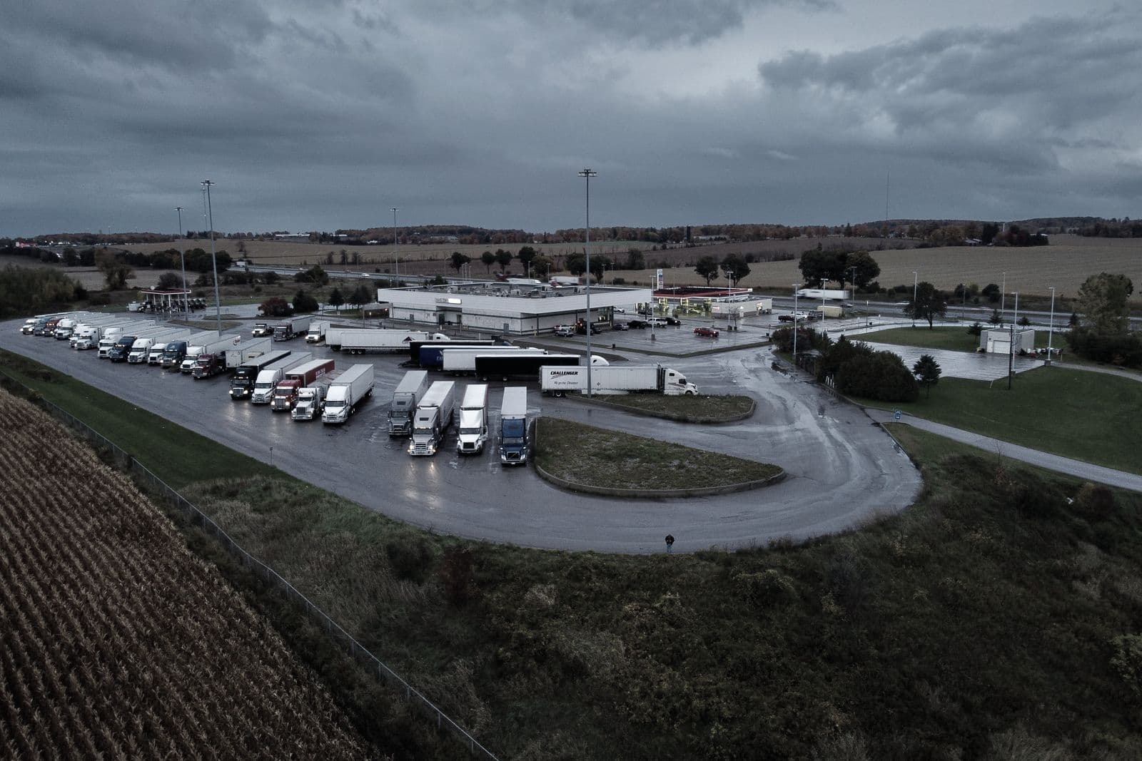 Vista aérea de un área de servicio junto a la autopista con camiones aparcados al anochecer