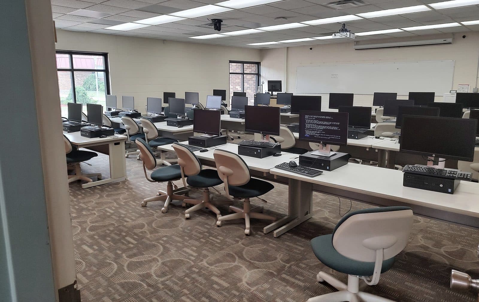 Aula de informática con filas de puestos y sillas, sin personas
