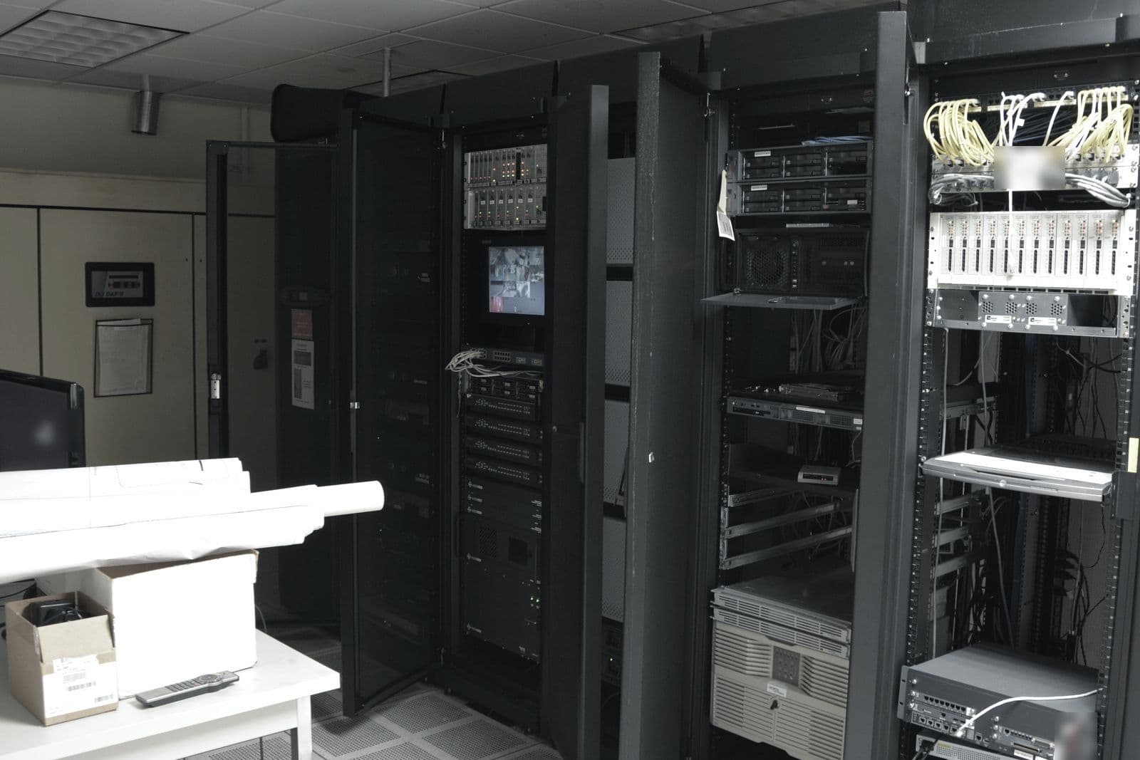 Sala técnica de empresa con armarios rack abiertos, servidores, cableado y suelo técnico